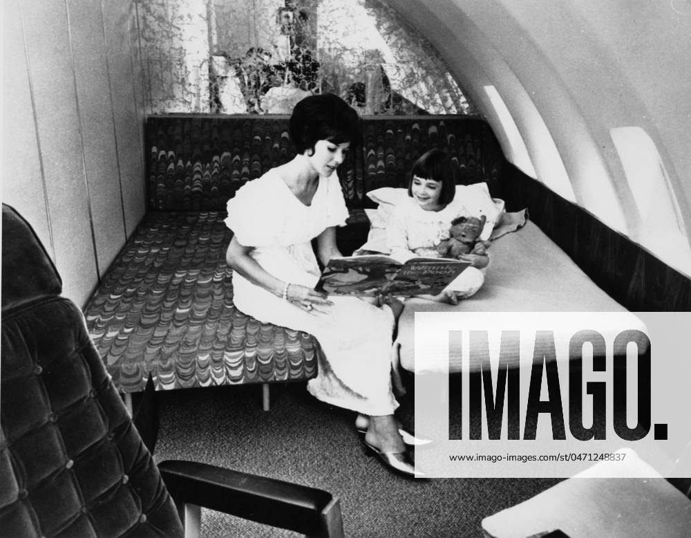 JUMBO JET BEDTIME STORY Even on board a Boeing 747 Jumbo Jet , this young mother takes time to don her gold slippers and read a bedtime story (Winnie the Pooh, what else?) to her young daughter. Date: 1960s