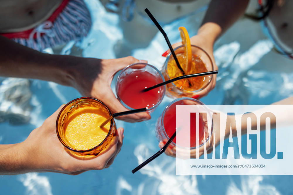 Close-up of female and male hands holding glasses with iced cocktails and clinking them Close-up of female and male hands holding glasses with iced cocktails and clinking them. Friends make festive toast with delicious drinks against background of clear blue pool water. Party, vacation.