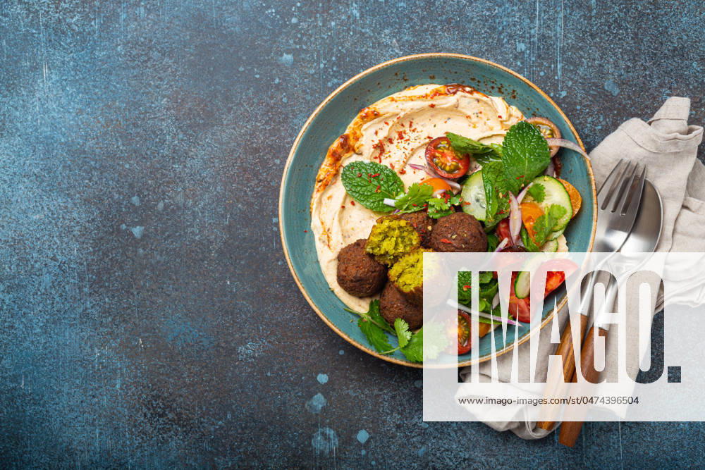 IMAGO Creative, Food, Hummus Middle Eastern Arab meal with fried falafel, hummus, vegetables salad space for text Middle Eastern Arab meal with fried falafel, hummus, vegetables salad with fresh green cilantro and mint leaves in ceramic bowl on stone rustic background top view. Arabic cuisine, space for text