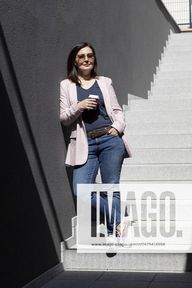 Smiling Beautiful Brunette Woman Hold Paper Cup Of Coffee Standing On Stairs Near Office Outdoor, Dressed In Stylish Casual Clothes, Summer Sunny Day. Taking A Break. Lifestyle Portrait Mature Female. Smiling Beautiful Brunette Woman Hold Paper Cup Of Coffee Standing On Stairs Near Office Outdoor, Dressed In Stylish Casual Clothes, Summer Sunny Day. Taking A Break. Lifestyle Portrait Mature Female
