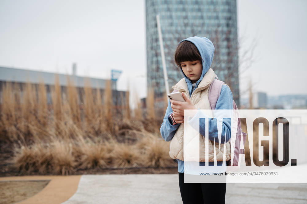 Girl standing outdoors, scrolling on smartphone. Using social media. Online bullying or cyberbullying for young schoolgirl. Girl standing outdoors, scrolling on the smartphone. Using social media. Online bullying or cyberbullying for young schoolgirl. model released