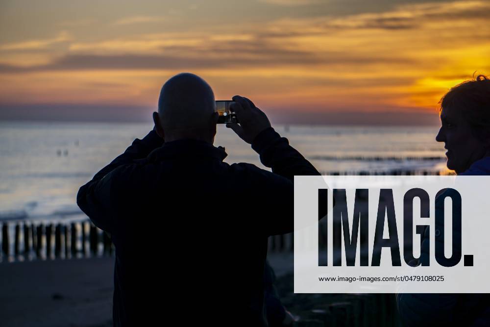Sunset on the beach of Zoutelande, beach with wooden pile breakwaters, tourists, Zeeland, Netherlands Sunset Zeeland