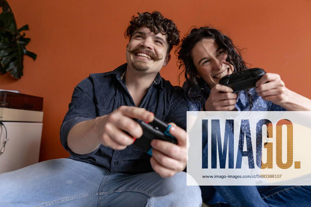 IMAGO Creative, Lifestyle, Gaming Cheerful couple playing video game at home model released, Symbolfoto property released, JOSEF24254