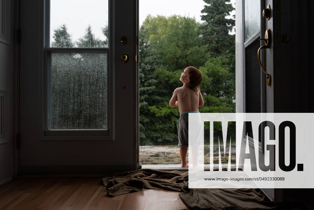 Child stands in doorway looking out at rainy scene with wet trees. Wingham, Ontario, Canada CR_ATBL240528-1433674-01 ,model released, Symbolfoto