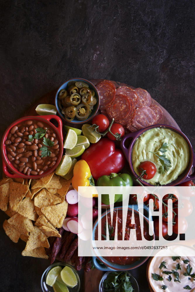 Mexican theme charcuterie board grazing platter with guacamole, salsa, beans, jalapenos, chorizo, and tortilla chips. Negative copy space. Mexican theme charcuterie board grazing platter with guacamole, salsa, beans, jalapenos, chorizo, and tortilla chips. Negative copy space.
