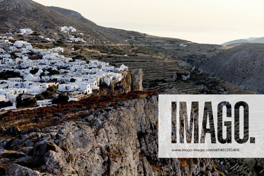 A scenic view of a traditional white village nestled in rugged hills, bathed in the warm glow of the setting sun. Folegandros Greece bola01007