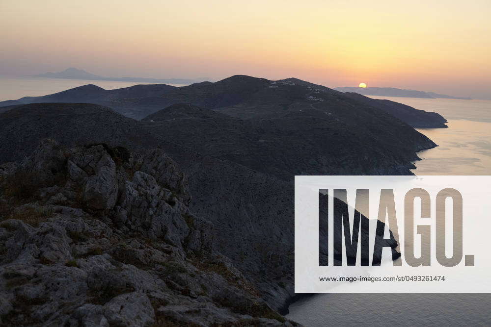 The sun sets behind a mountainous coastline, casting a warm glow over the serene seascape. Folegandros Greece bola01010