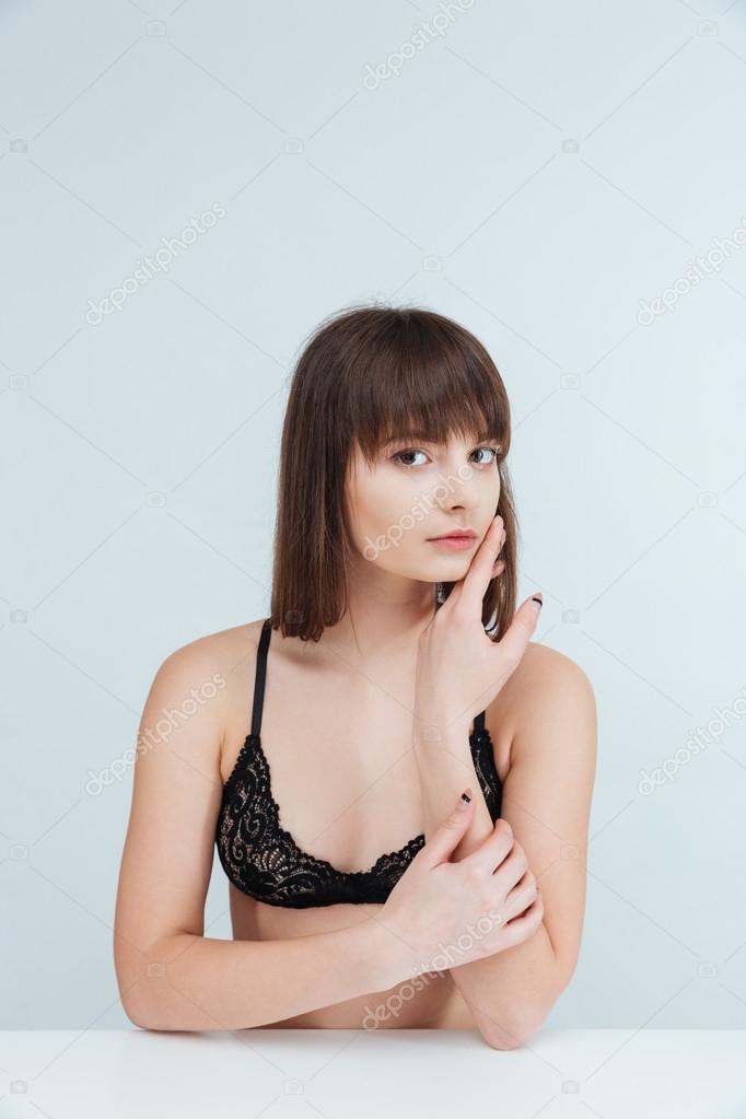 Attractive young woman in lingerie sitting at the table and looking at camera isolated on a white backround model released