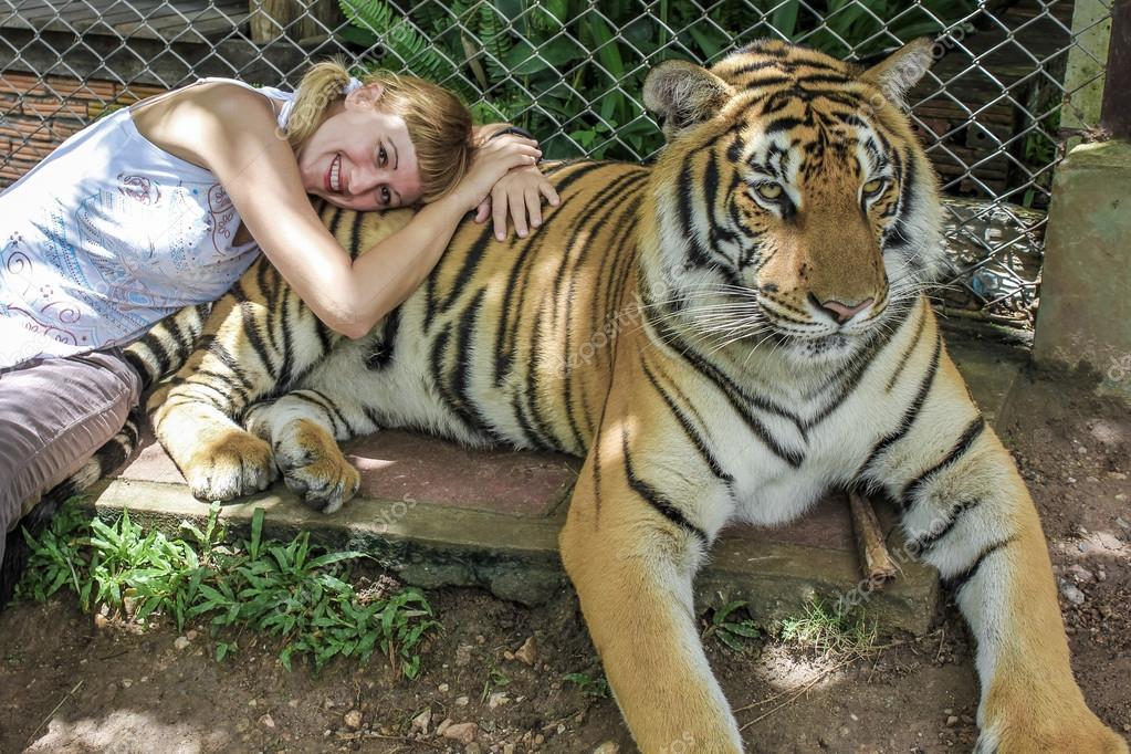 Smiling blonde tourist woman lying on a adult tiger, Zoo of Chiang Mai, Thailand, Asia. model released