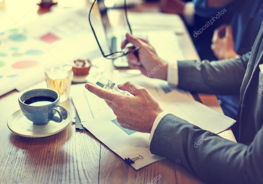 Businessman using smartphone while sitting at the desk with documents and cup of coffee during meeting. original photoset