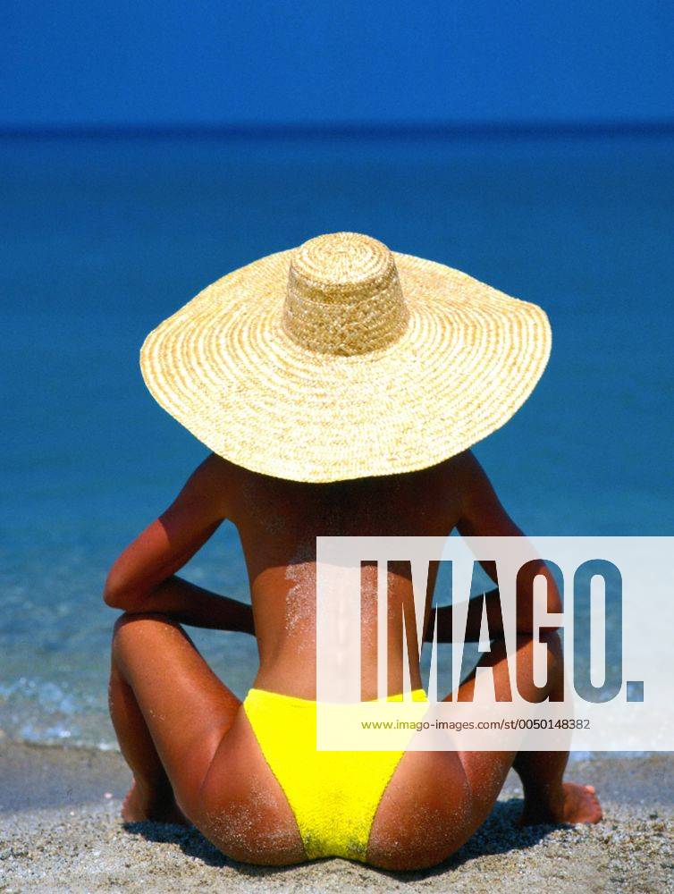 Junge Frau mit Sonnenhut schaut aufs Meer