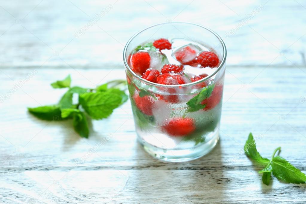 Glass of cold refreshing summer drink with berries and ice cubes on table close up