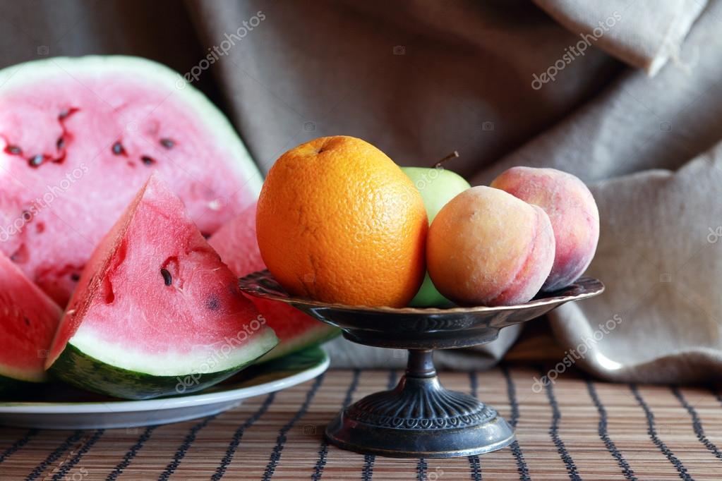 Still life with various fruits in metal bowl near sliced watermelon