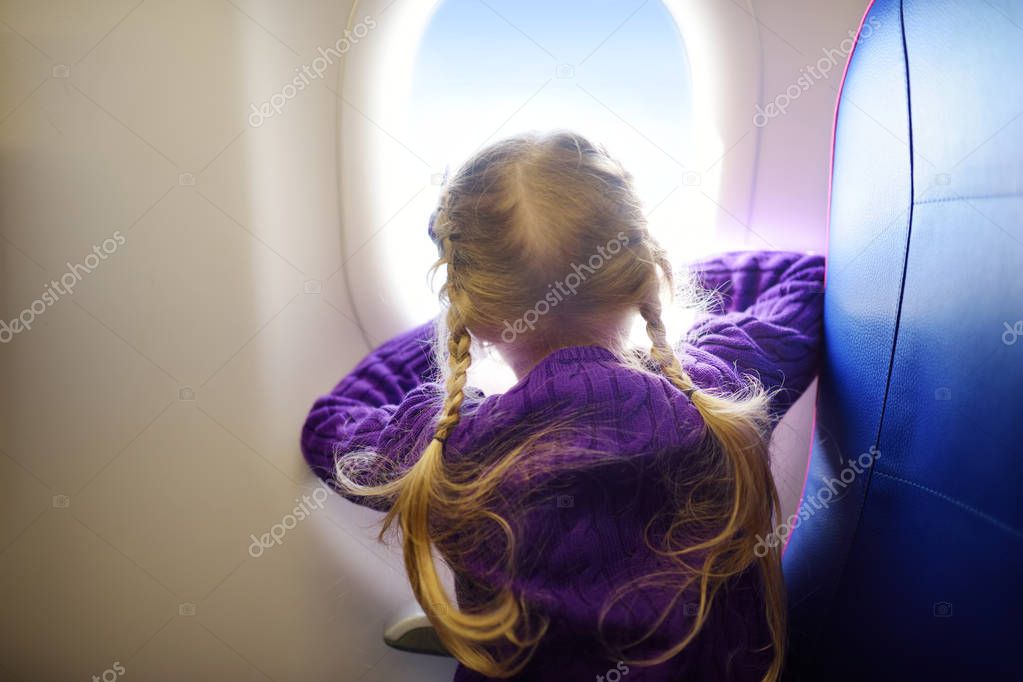 Adorable little girl traveling by an airplane. Child sitting by aircraft window and looking outside. Traveling with kids abroad. model released