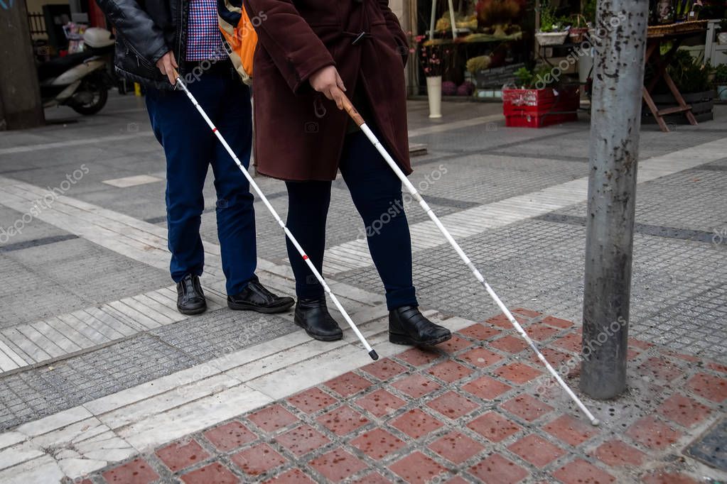 Blind man and woman walking on the street using a white walking stick