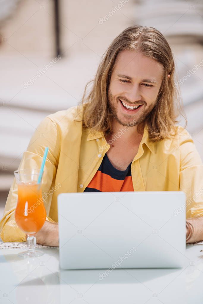 Smiling young man using laptop while sitting outdoors at sunny day model released