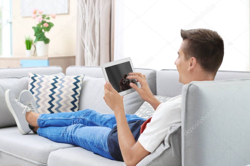 Young man using tablet computer on sofa at home model released