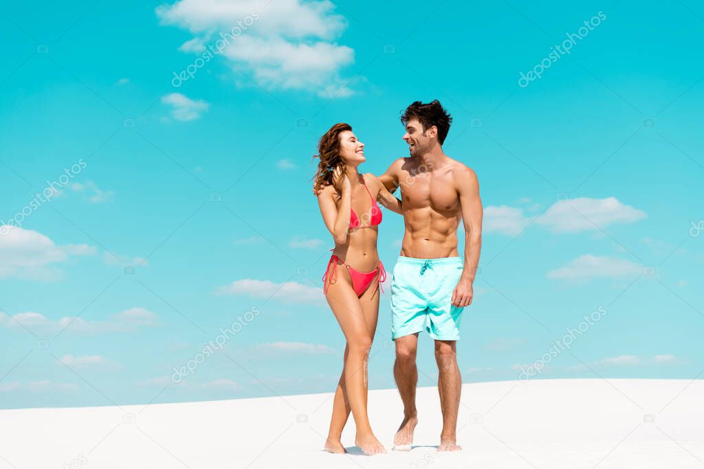 Smiling young couple looking at each other on sandy beach model released