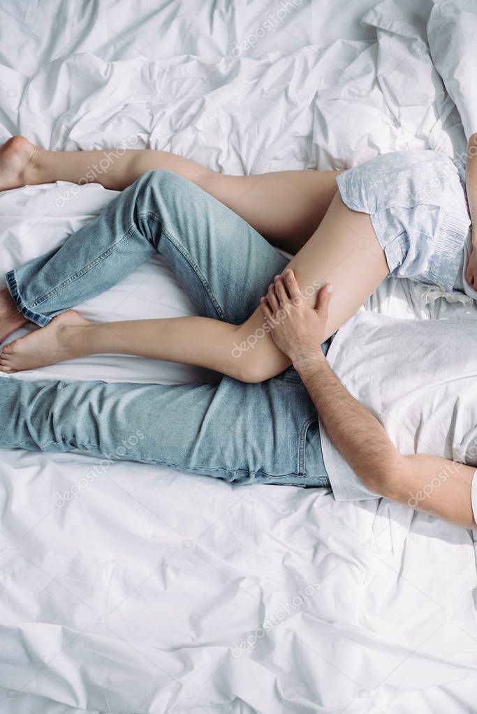 Cropped view of woman in shorts and man in jeans hugging and lying on bed