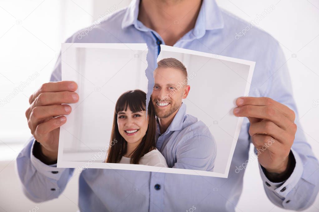 Close-up Of A Man's Hand Tearing Photo Of Smiling Couple In Two Pieces model released