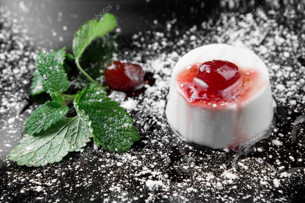 Photo of italian panna cotta dessert with strawberry sirup and mint leaf on the black wooden background
