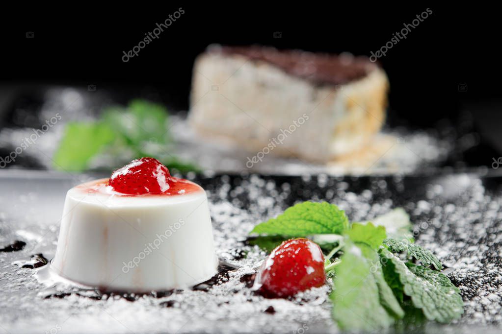 Photo of italian panna cotta dessert with strawberry sirup and mint leaf on the black wooden background