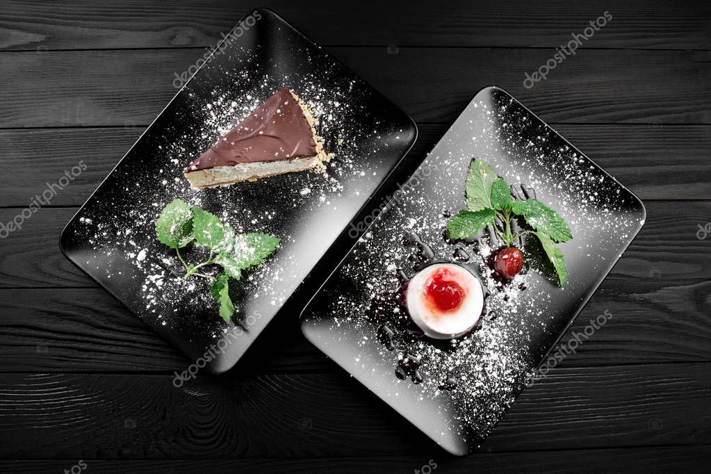 Photo of italian panna cotta dessert with strawberry sirup and cake with nuts and chocolate on the black plate on dark wooden background