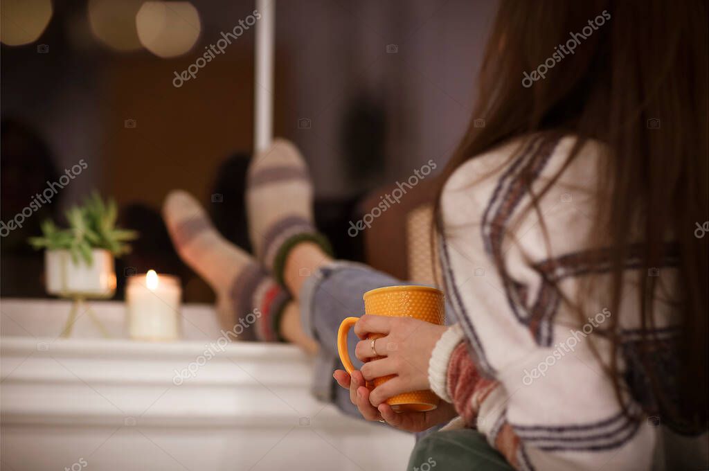 Back view of unrecognizable woman in warm clothes enjoying hot beverage and relaxing in cozy room in evening at home model released