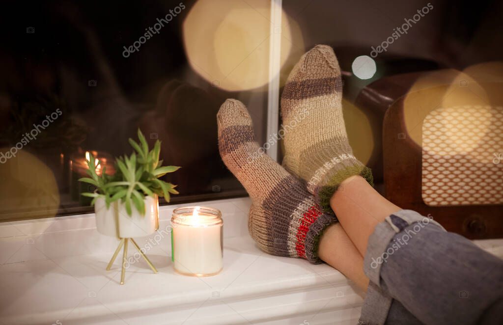 Back view of unrecognizable woman in warm clothes relaxing in cozy room in evening at home. Close up model released