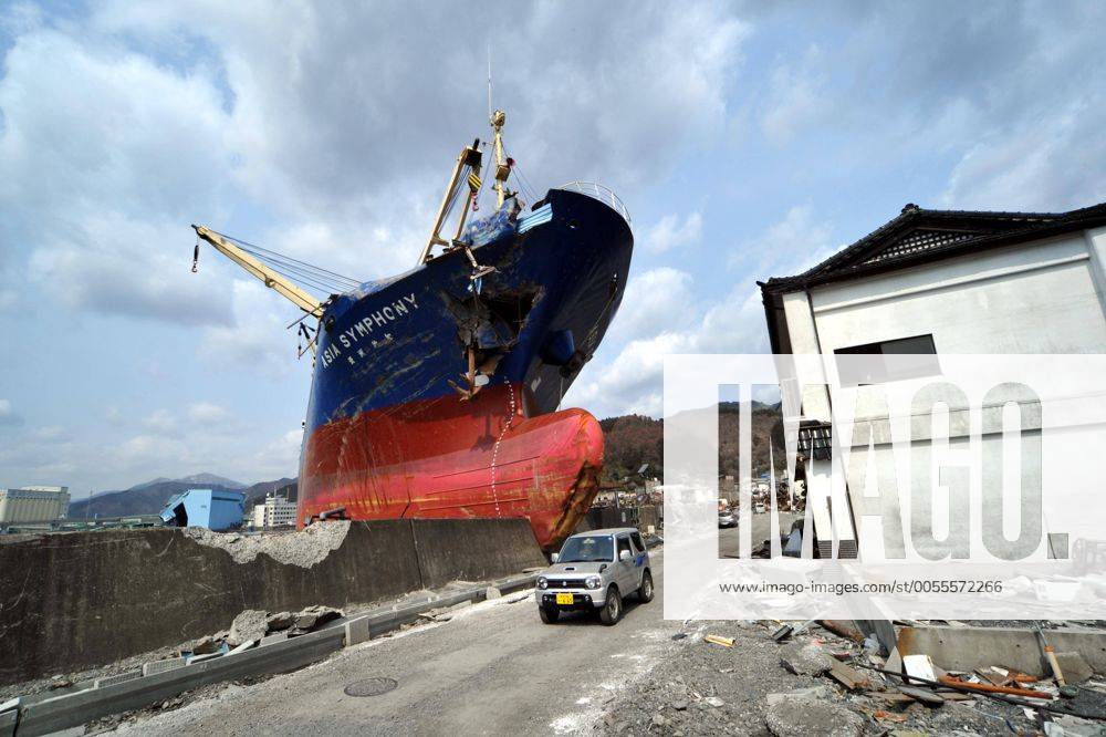 April 1st, 2011, Kamaishi, Japan - A small van goes by the looming bow of Asia Symphony, a Panamanian ocean going vessel being left aground on the wharf in the port of Kamaishi , Iwate Prefecture, on April 1, 2011, three weeks after this major northeastern Japanese port was destroyed by a magnitude 9.0 earthquake and ensuing tsunami. (ayfa004588)