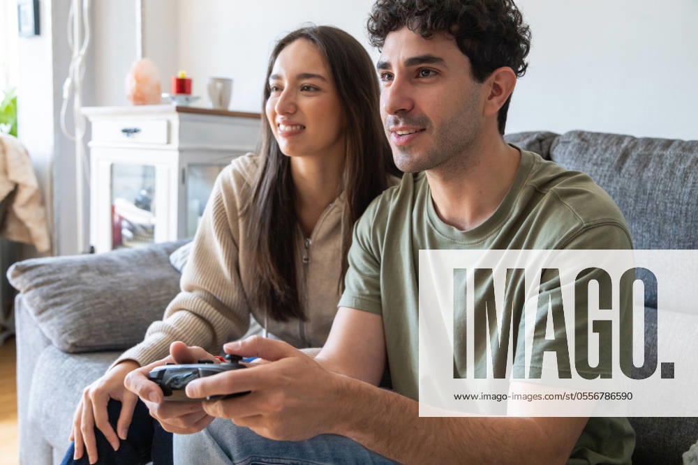 Young, happy couple sitting on a sofa, engaged in playing a video game They enjoy a cozy, casual moment in a well-lit, comfortable living room setting Model Released IgnacioFerrandiz_ID21881_641140_015