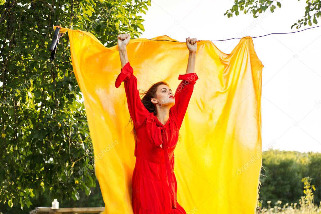 Woman in a red dress with hands raised up yellow fabric nature. High quality photo model released