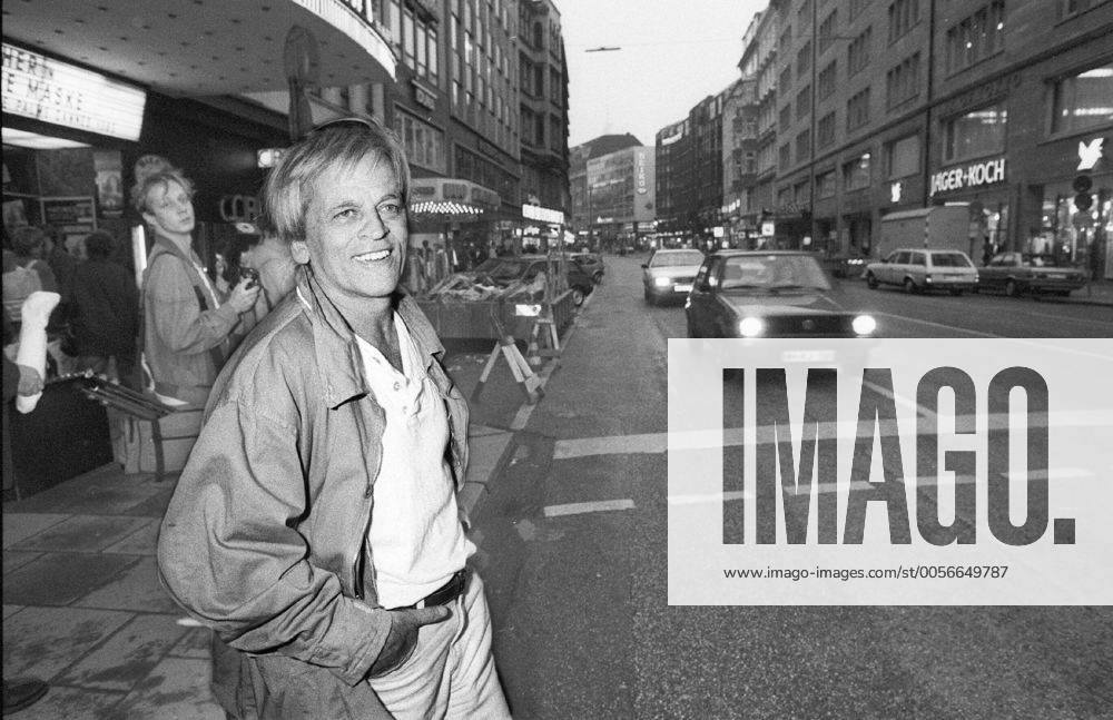 Klaus Kinski (Schauspieler) 10 85 vZ Klaus Kinski im Oktober 1985 in Hamburg Deutschland deutsch Deutscher Mann Schauspiel TV Fernsehen Film Kino Autor grauhaarig weisshaarig kurzhaarig leger Jacke Hemd quer halb stehend draußen lächelnd Stadt Innenstadt Straße Autos PKW fahrend sw