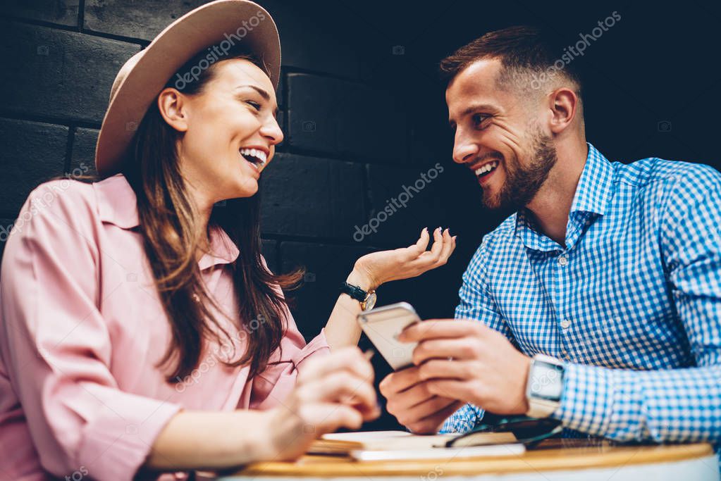 Cheerful male and female friends enjoying free time together joking and share multimedia in networks during meeting in cafe, romantic couple laughing viewing funny photos on mobile phone during date model released