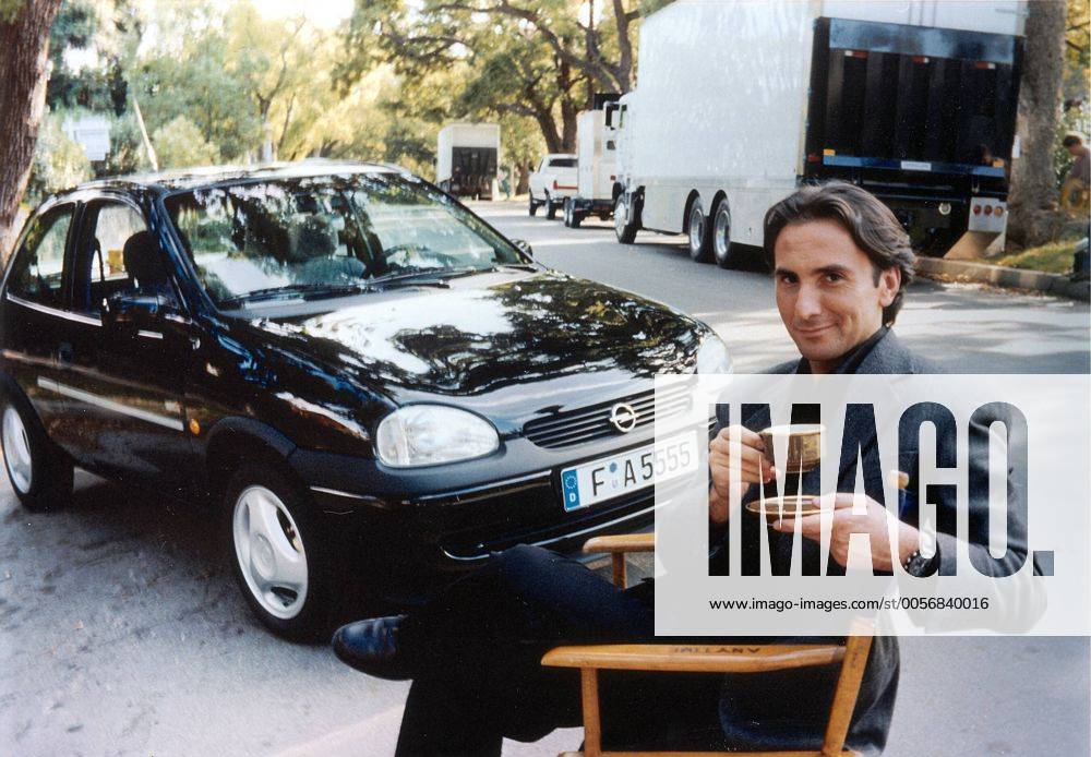 Bruno Maccallini (Schauspieler) 03 97 teu Mann TV Fernsehen Schauspiel Regisseur Regie Autor Werbung Werbefigur Angelo Capuccino Nestlé Reklame Kaffee Kaffeewerbung Opel Corsa actor director writer author draußen quer halb sitzend lächelnd Kaffeetasse Tassee Auto Kfz PKW