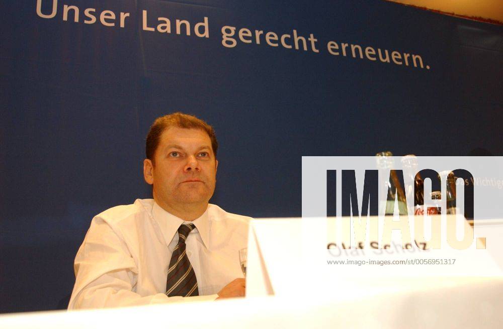 Olaf Scholz (Politiker) 02 04 wow Mann Politik Politiker Partei SPD Generalsekretär Rücktritt Bekanntgabe Ankündigung angekündigt am 6. Februar 2004 dunkelhaarig kurzhaarig leger Hemd Krawatte halb quer sitzend lächelnd Podium Namensschild Schild Name Slogan Unser Land gerecht erneuern Fototermin am 05.02.2004 in Gütersloh
