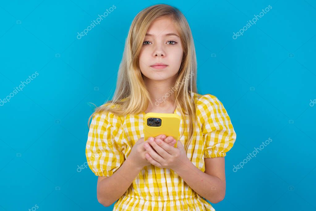 Portrait of serious confident beautiful caucasian girl wearing dress holding phone in two hands model released