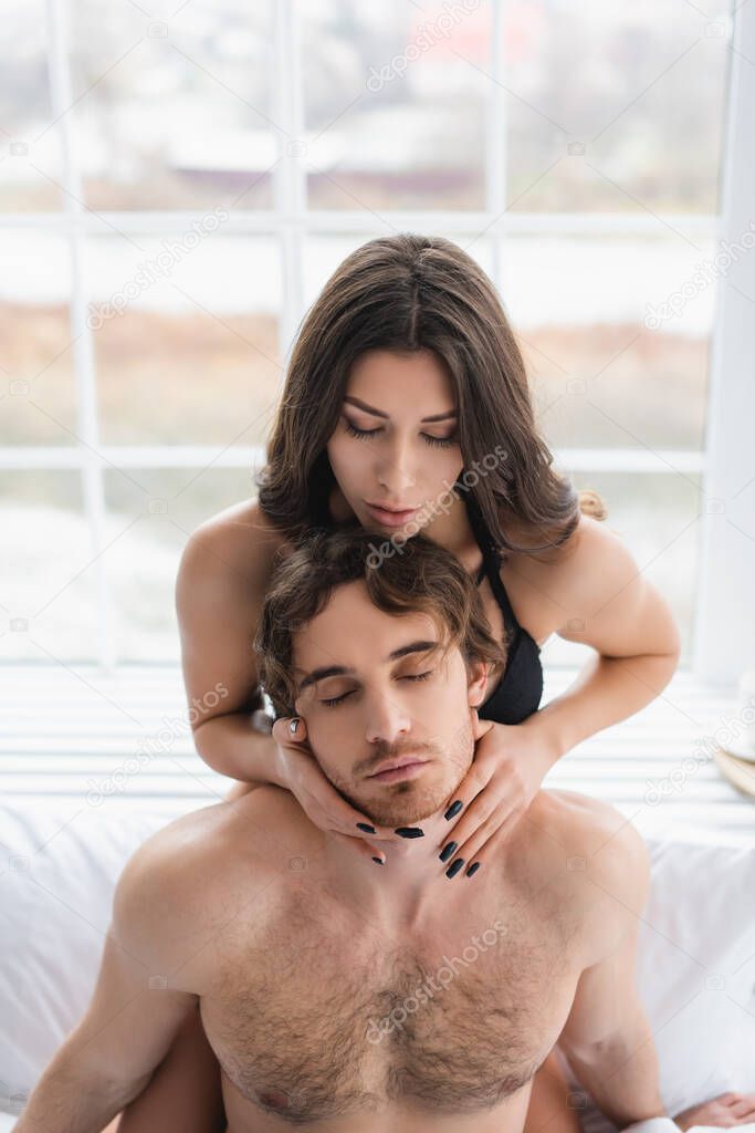 Sexy woman touching neck of muscular boyfriend in bedroom model released
