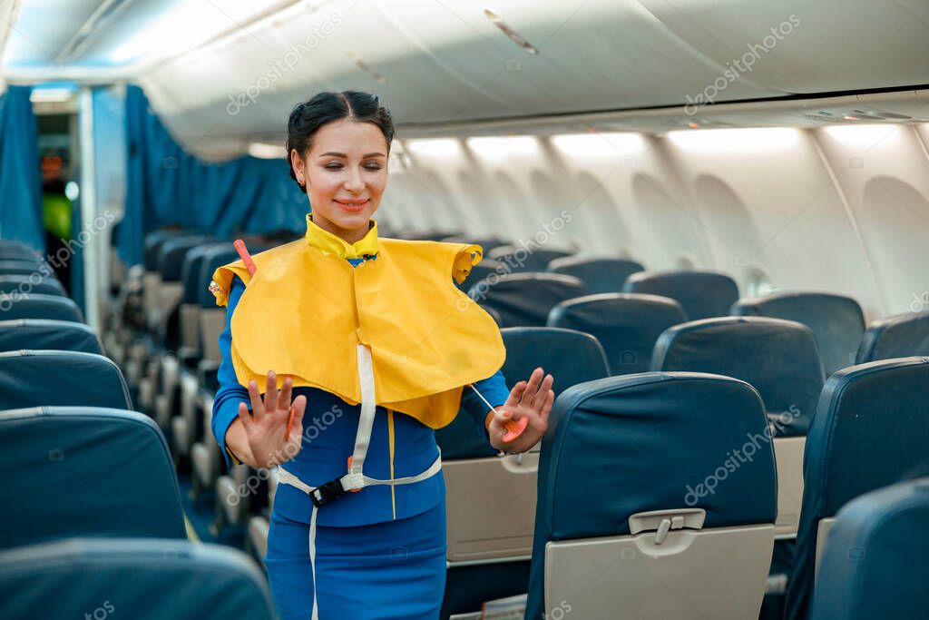 Smiling woman stewardess or air hostess wearing safety vest while standing in aircraft passenger cabin model released