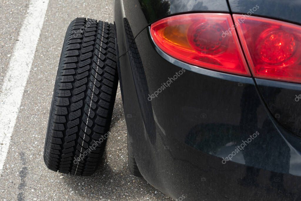 Picture of black car's brand new tyre on the road on a summer day