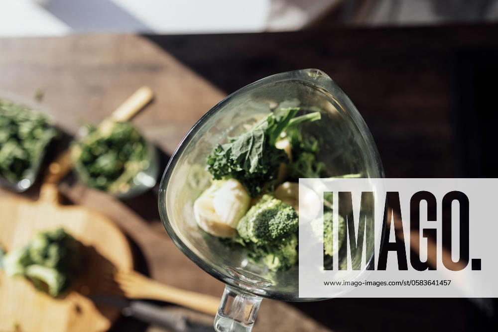 Close-up of green vegetables, banana and herbs in a blender. Wavy cabbage, broccoli and arugula on a wooden table. Top view. Preparation of a vitamin smoothie. Close-up of green vegetables, banana and herbs in a blender. Wavy cabbage, broccoli and arugula on a wooden table. Top view. Preparation of a vitamin smoothie. Healthy food and drinks.