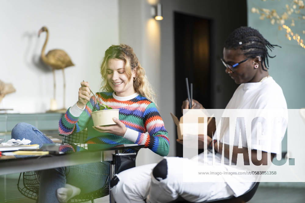 A happy young multiethnic couple takes a break from smart working at home, enjoying a meal together in a cozy, modern interior with nature illustrations Model Released VictorCuenca_ID22085_646426_029