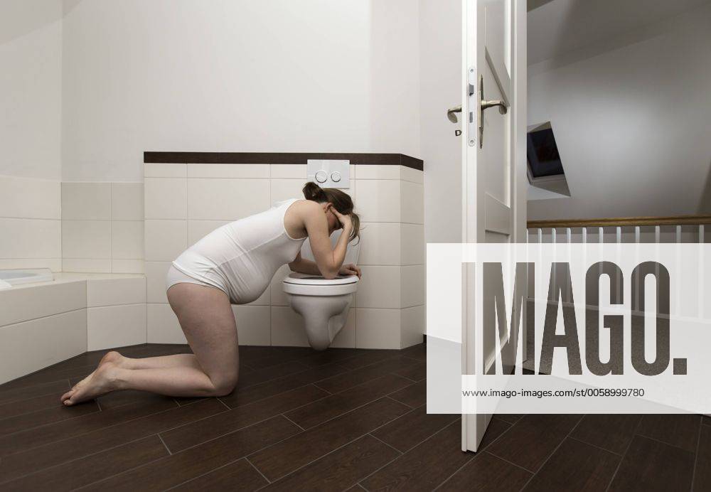 Junge schwangere Frau, 35 Jahre alt, beugt sich wegen Übelkeit über eine Toilette. Young pregnant woman, 35 years old, feeling sick on a toilet. Schwangere Frau beugt sich wegen Übelkeit über eine Toilette Pregnant woman feeling sick on a toilet