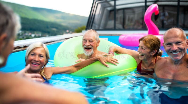 Group of cheerful seniors in swimming pool outdoors in backyard, talking., Group of cheerful seniors in swimming pool outdoors in backyard, talking and having fun.