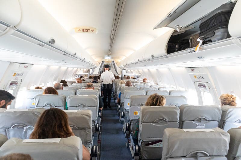 Interior of commercial airplane with passengers on their seats during flight., Interior of commercial airplane with unrecognizable passengers on their seats during flight. Steward in blue white uniform walking the aisle of commercial airplane.
