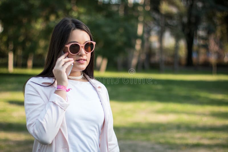 Young woman having a conversation on her smartphone, A young woman having a conversation on her smartphone outdoors in a park on a sunny day. model released