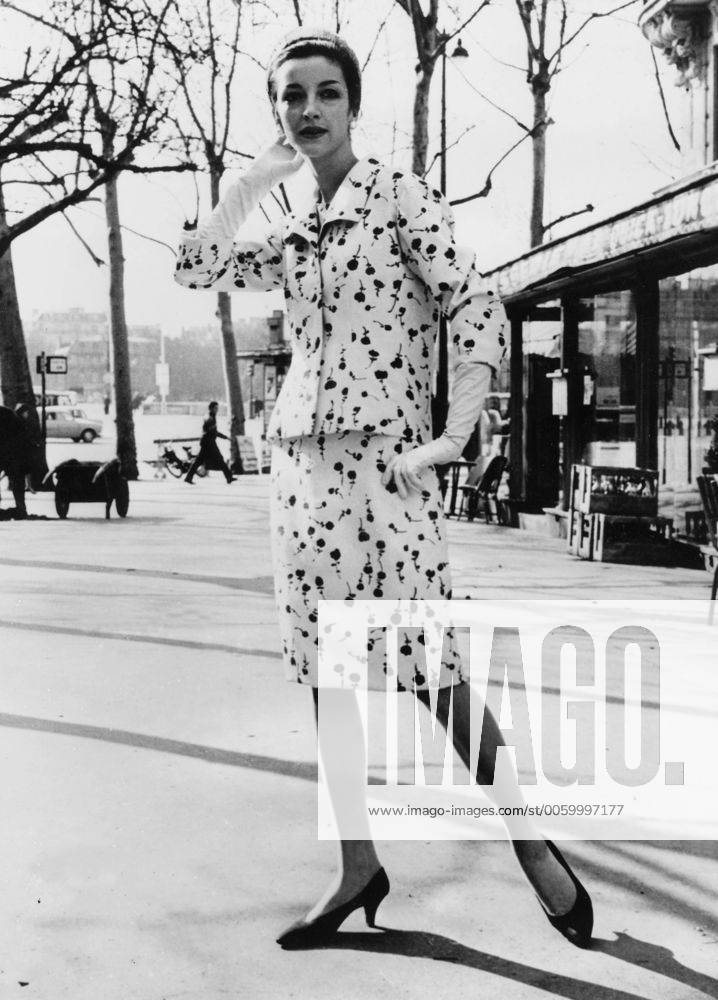 Paris Spring ensemble by Givenchy for this coming season. Medium is blue flowered printed white shantung. The material is softly gathered in the back. The long sleeved wide collared jacket stops at the hip line and is held tight by four white shantung covered buttons in front. A navy blue straw hat and white kid gloves complete the ensemble 1965 UnitedArchives00507316