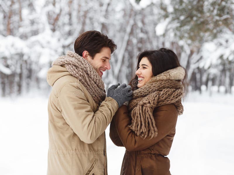 Loving Couple Holding Hands Standing Having Romantic Winter Date Outside, Loving Couple Holding Hands Standing In Snowy Park Having Romantic Winter Date Outside. New Year Morning Concept.