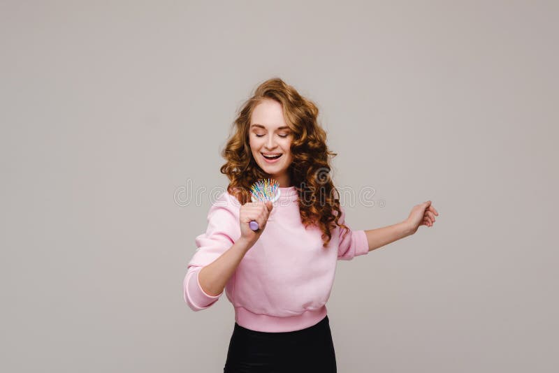 Joyful girl sings into a microphone. Girl fooling around and using a comb instead of a microphone, Joyful girl sings into a microphone. Girl fooling around and using a comb instead of a microphone. model released