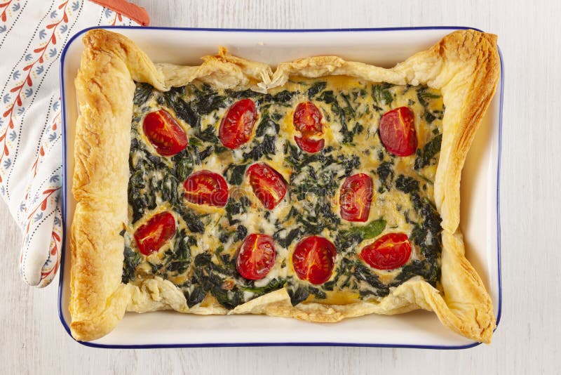 Home made spinach quiche top view, Vegetarian spinach pie or quiche with cheese and tomatoes in a baking dish from above